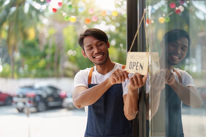 Young male manager in restaurant with tablet learning how to start a restaurant business. Man coffee shop owner with open sign. Small business concept